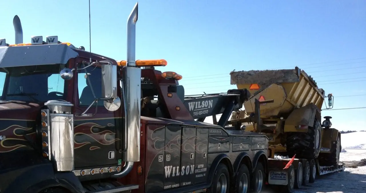 A Wilson's Towing wrecker hauling construction equipment on a lowboy trailer